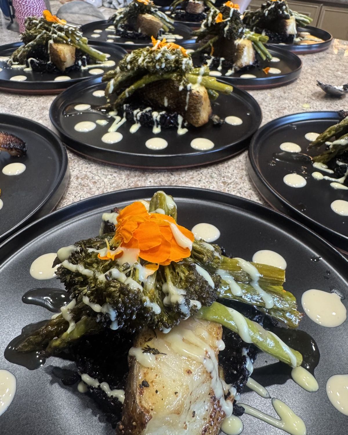 Row of plated seared fish courses with asparagus and edible flowers
