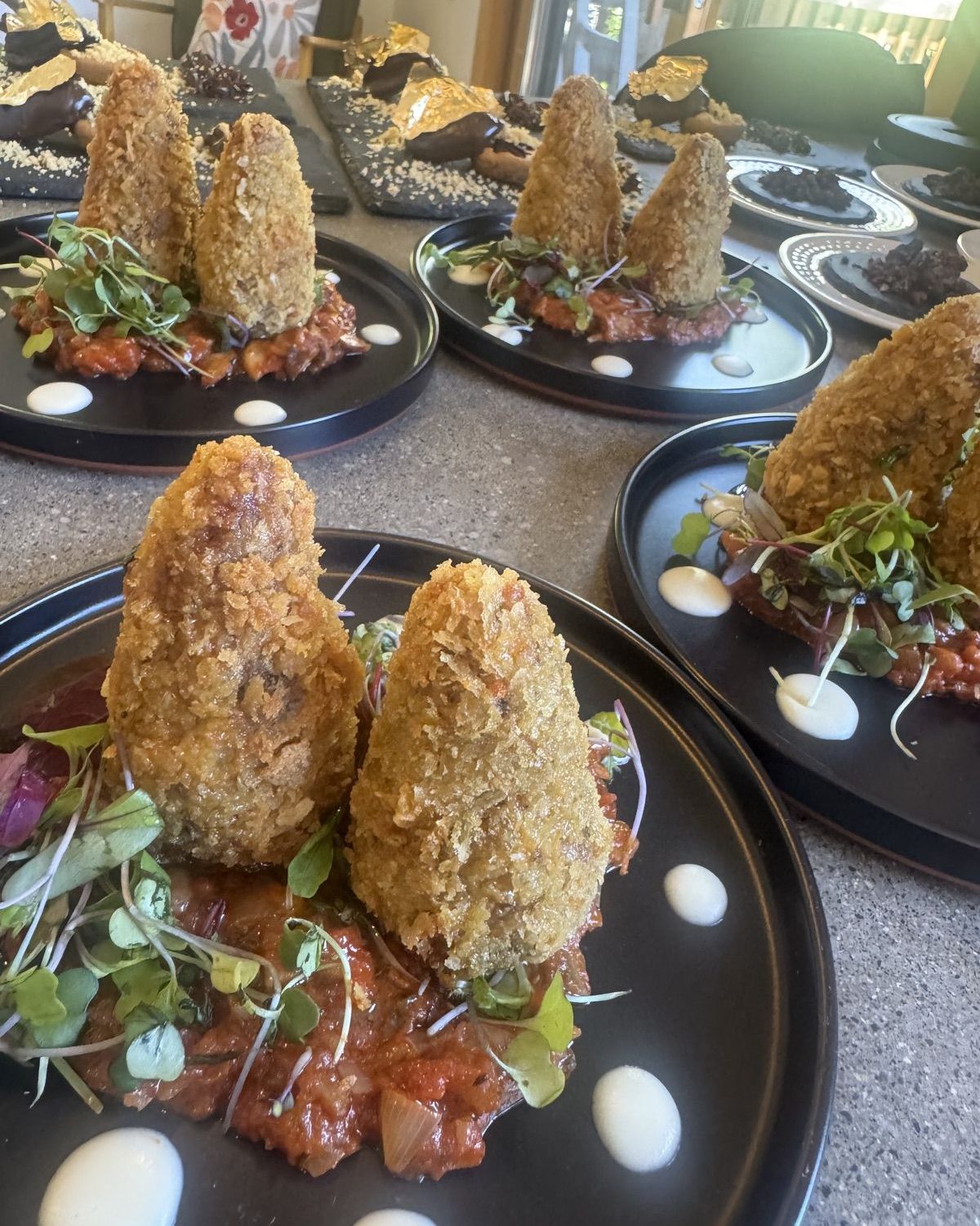 Breaded appetizers on black plates with red relish and sauce dots