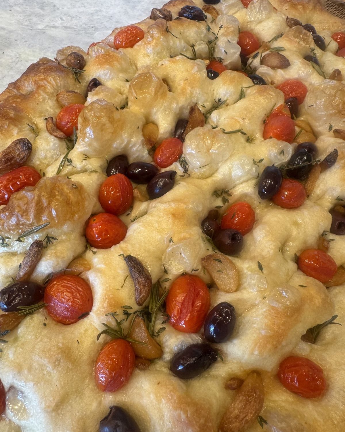 Focaccia topped with cherry tomatoes, olives, garlic, and rosemary