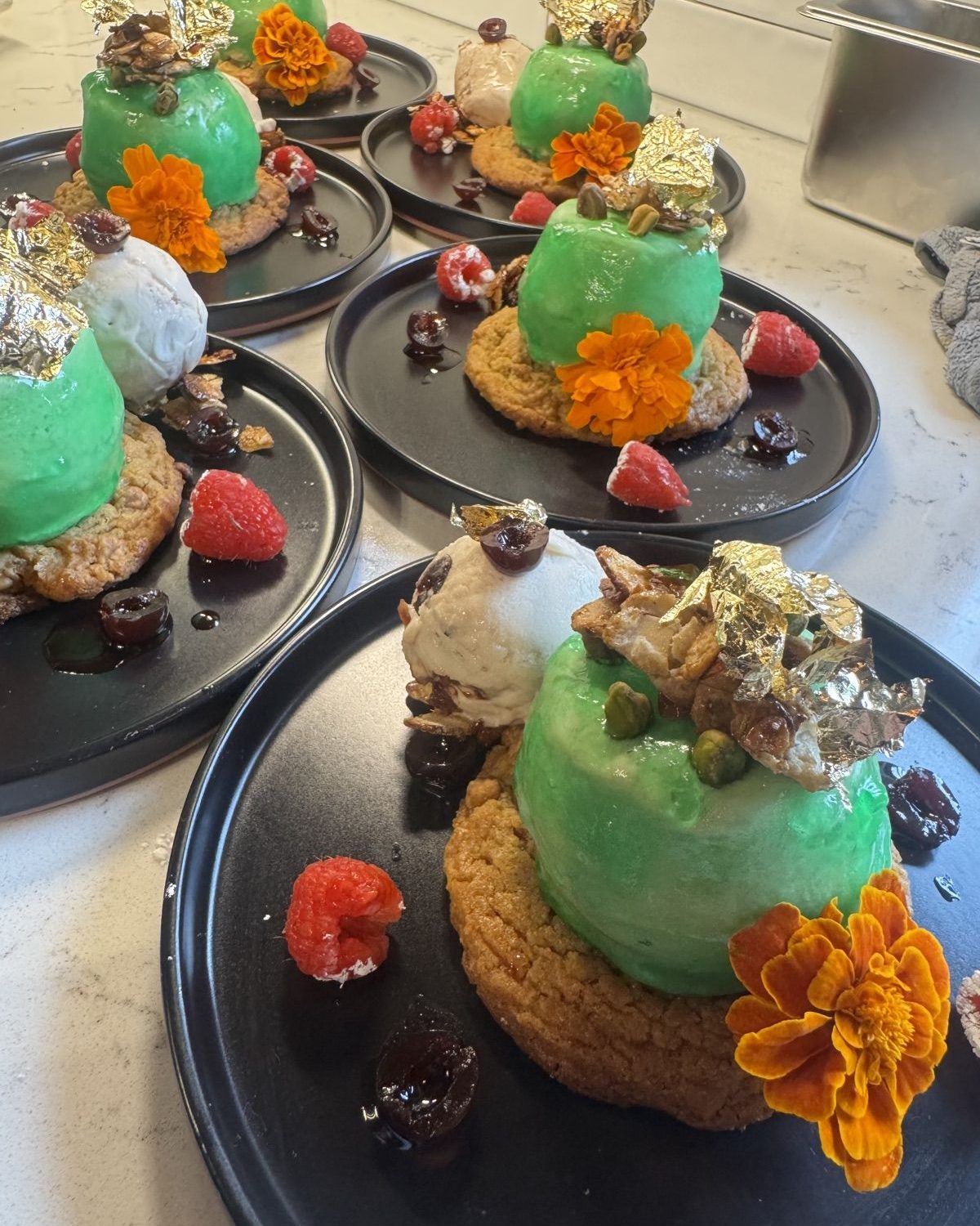 Green glazed dome desserts with gold leaf, flowers, and raspberries