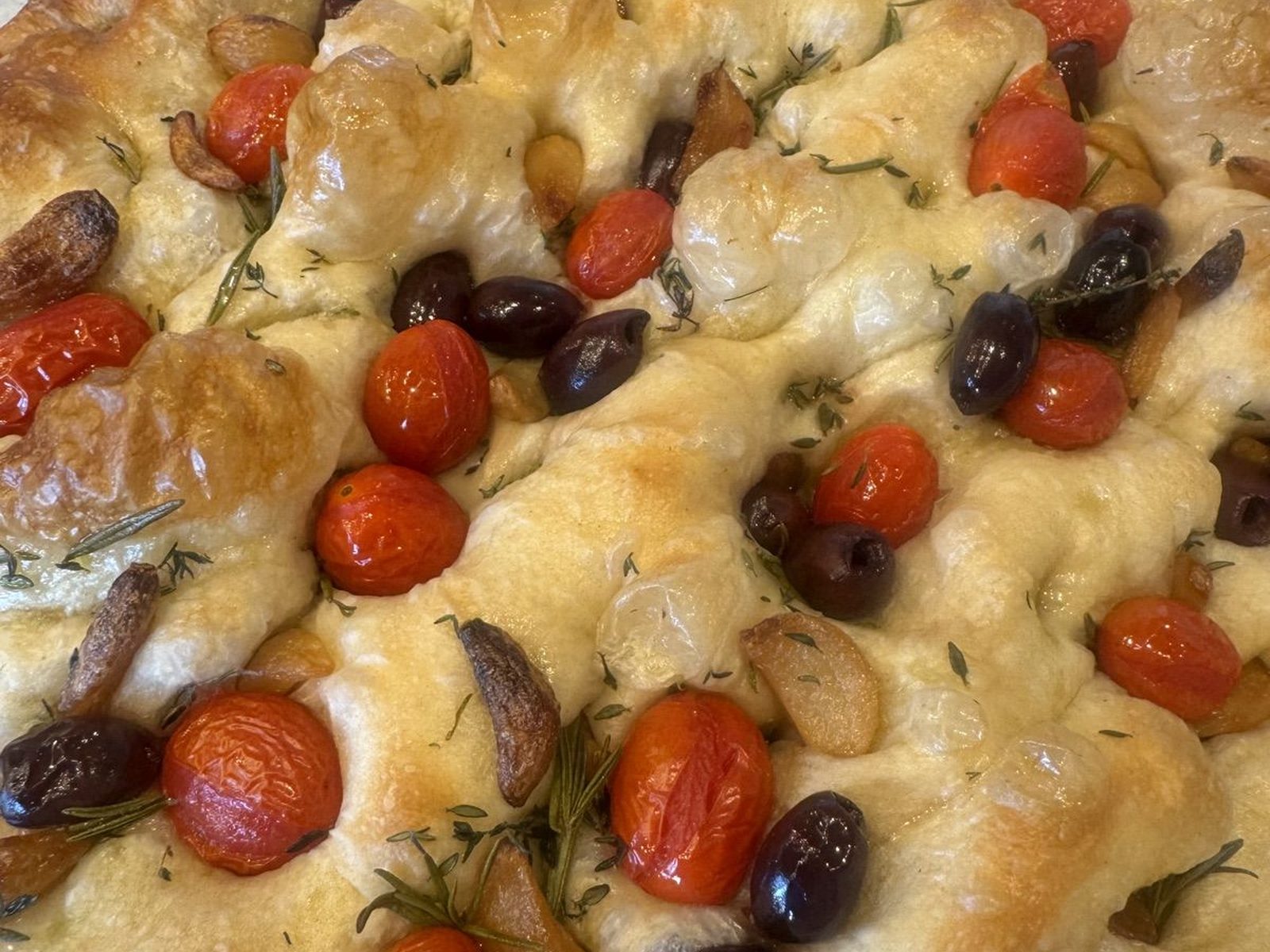 Focaccia topped with cherry tomatoes, olives, garlic, and rosemary