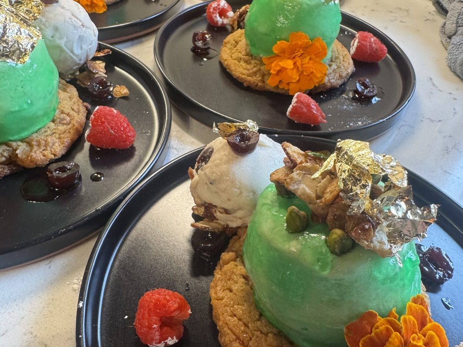 Green glazed dome desserts with gold leaf, flowers, and raspberries