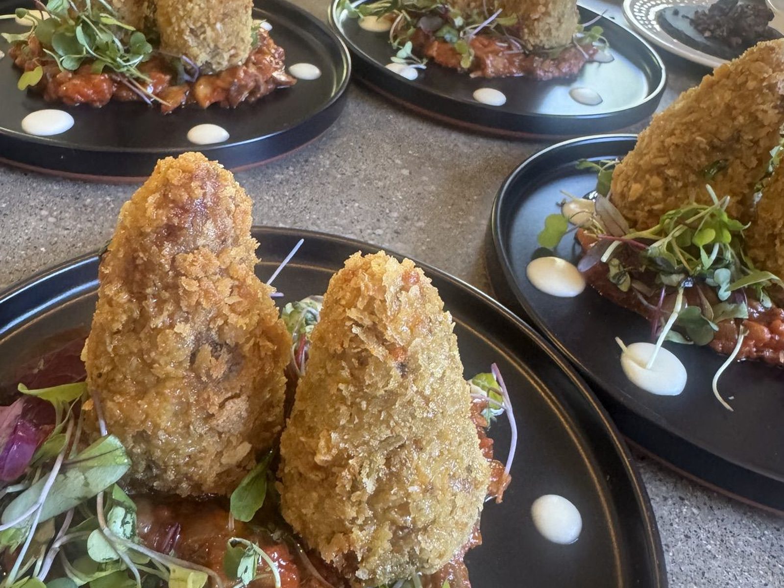 Breaded appetizers on black plates with red relish and sauce dots