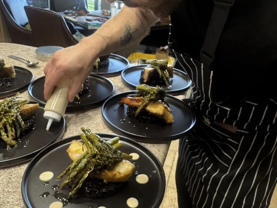 Chef Fikret Siler plating identical fish courses with sauce in a private home kitchen