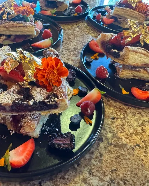 Layered berry pastry with fresh fruit and gold leaf on black plates