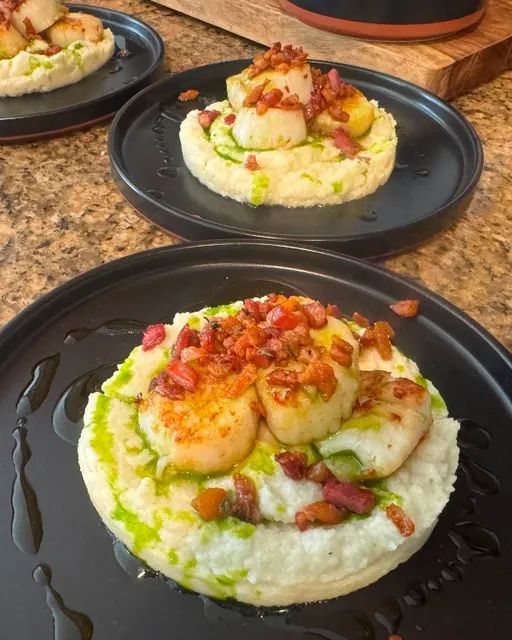 Seared scallops on white puree with green oil on black plates